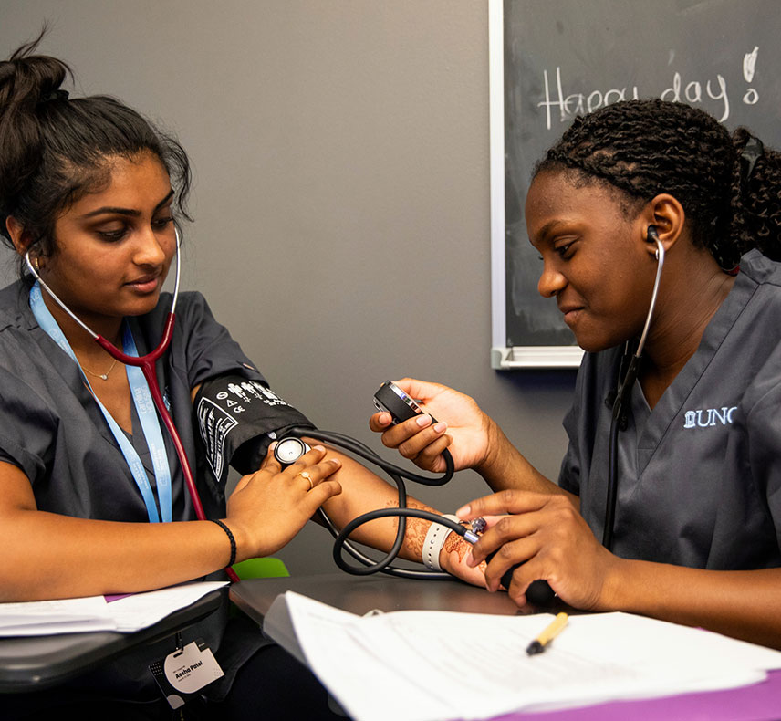 Two future medical students practising taking blood pressure in a classroom.